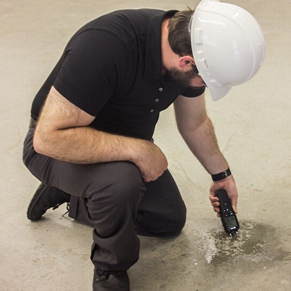 Man in een veiligheidshelm controleert restvocht in de vloer met een meetinstrument.